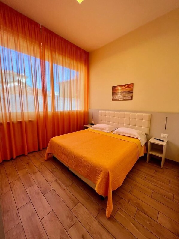 A hotel room with a large bed, wooden flooring, a nightstand, and a painting on the wall. - Casa Zeffirino (Sanremo)