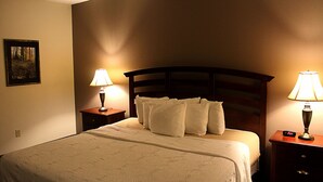 Una cama bien hecha con un cabecero, dos mesitas de noche con lámparas y un reloj de pared.