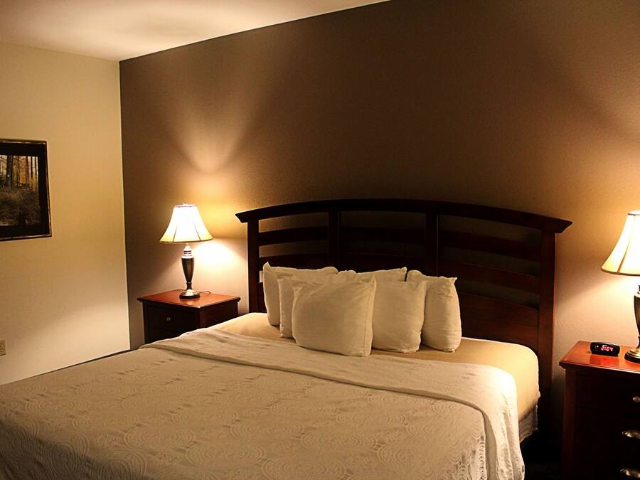 Una cama bien hecha con un cabecero, dos mesitas de noche con lámparas y un reloj de pared.