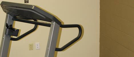 A treadmill in a room with carpeted flooring and a plain wall.