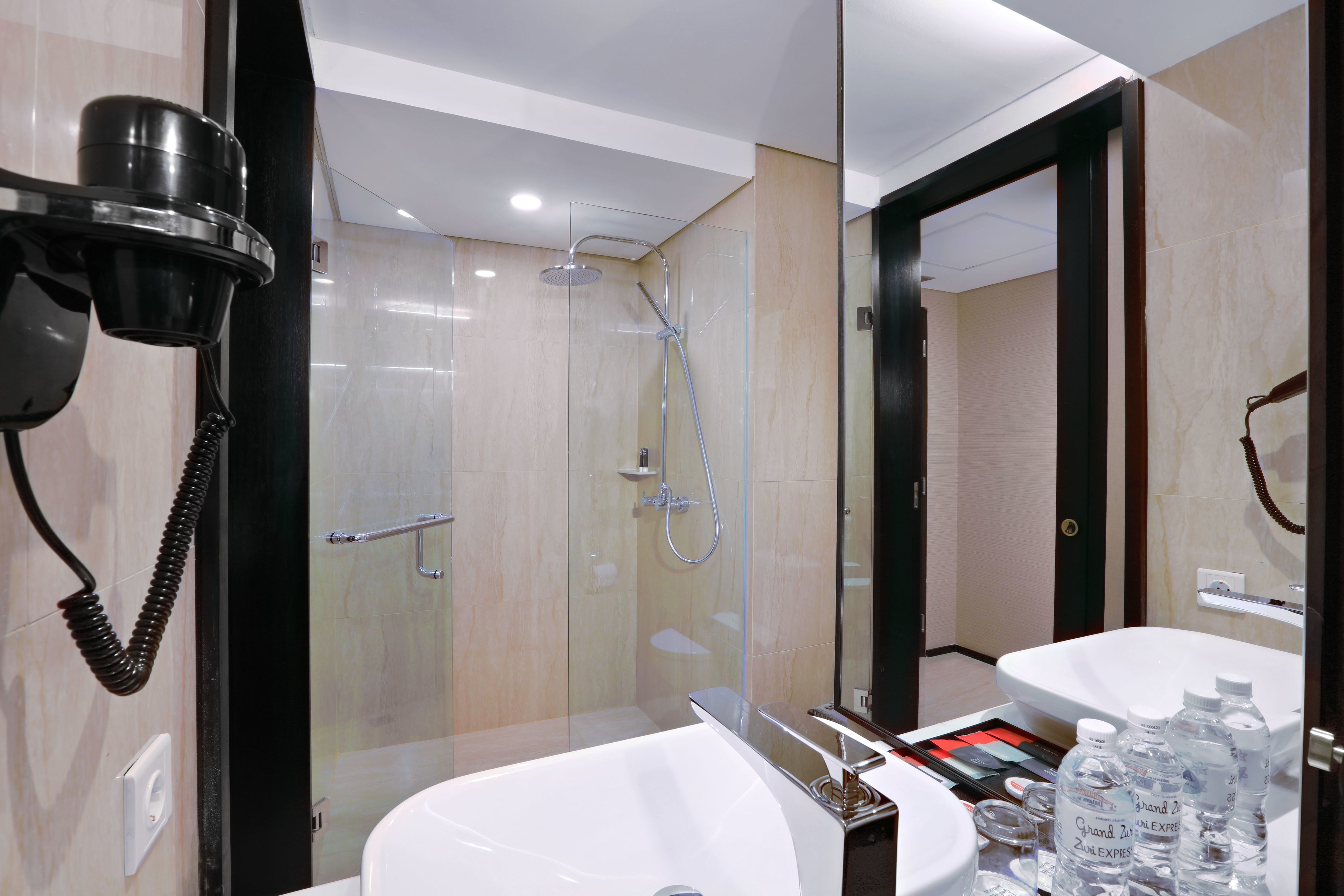 Un baño moderno con ducha envuelta en vidrio, un lavabo blanco y un secador de pelo fijado en la pared.