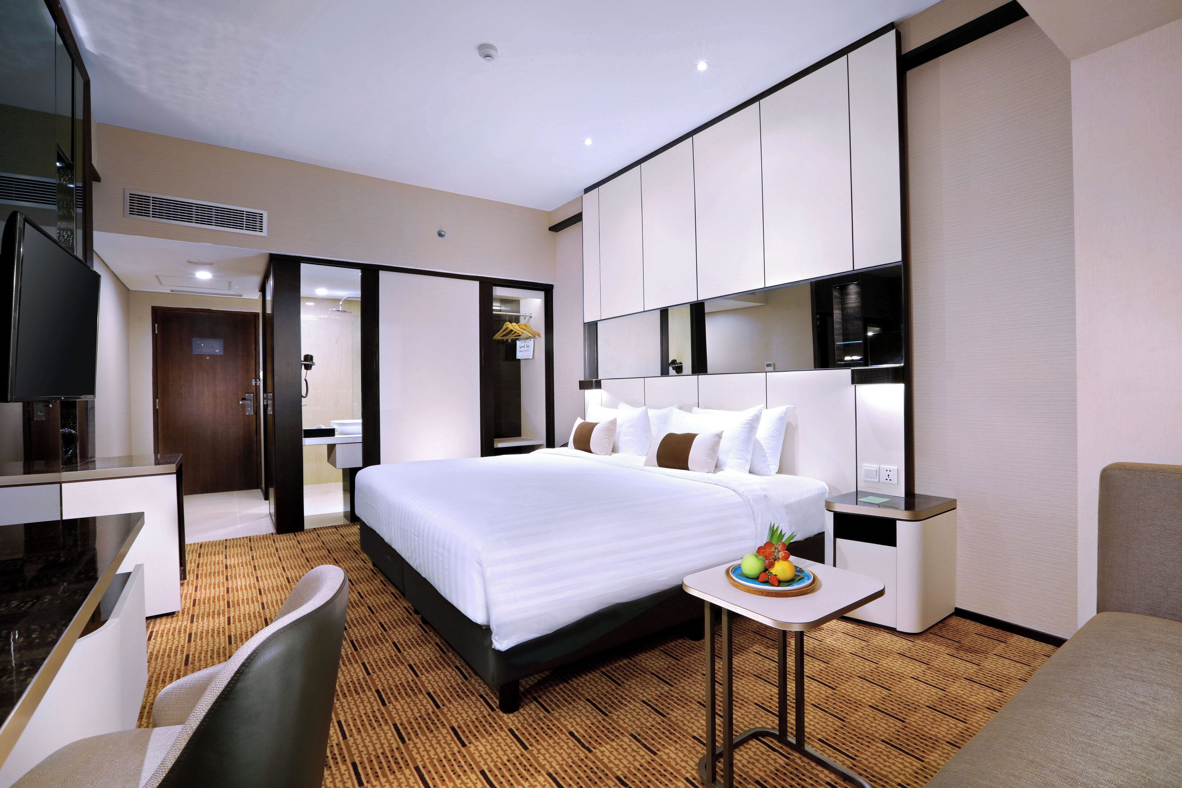 Habitación de hotel con cama, escritorio, silla, pequeña mesa con fruta y espejo.