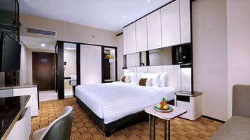 Habitación de hotel con cama, escritorio, silla, pequeña mesa con fruta y espejo.