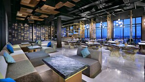 A modern lounge area with seating arrangements, tables, and a view of the cityscape through large windows. - The Alts Hotel (Palembang)