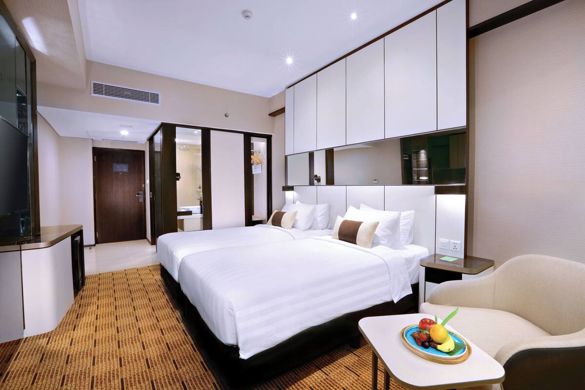 Habitación de hotel con una cama grande, una mesita de noche con frutero, una silla y un armario.