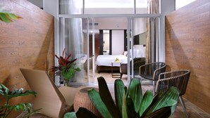A modern hotel room with a large sliding glass door leading to a balcony, wicker furniture, and a bed with a white duvet. - The Alts Hotel (Palembang)