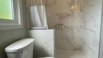 Un baño con inodoro, ducha con puerta de vidrio y paredes de mármol.