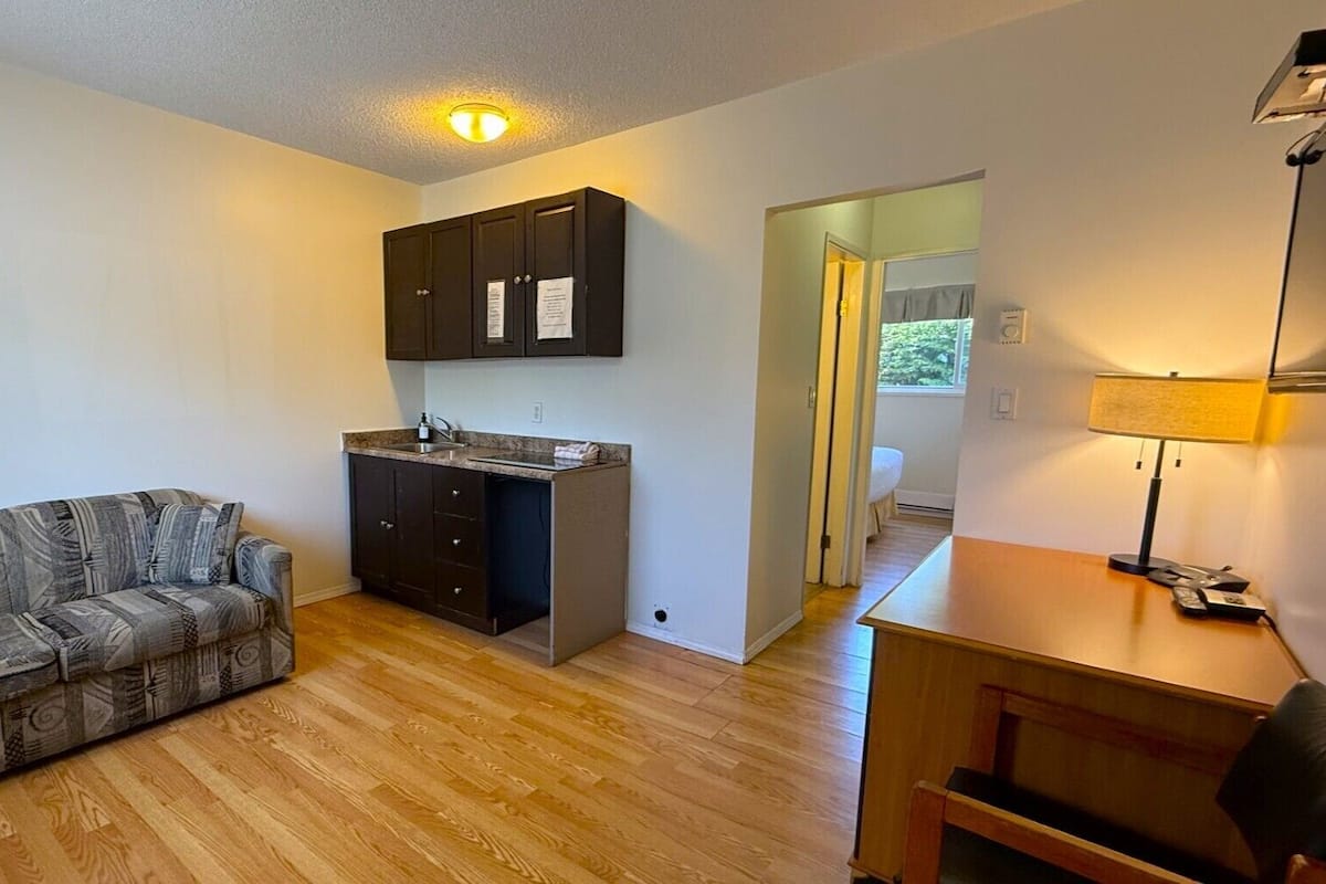 Un espacio habitable compacto con kitchenette, un sofá, un escritorio y una lámpara.