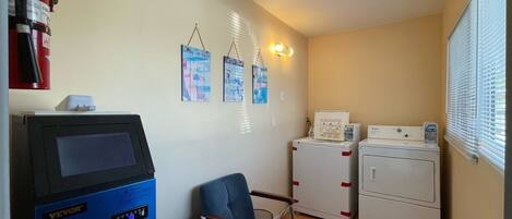 A laundry room with a blue appliance, a chair, and two stacked washing machines.