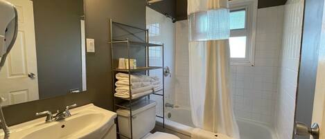 A bathroom with a sink, toilet, and bathtub. There is a shelf with towels and toiletries.
