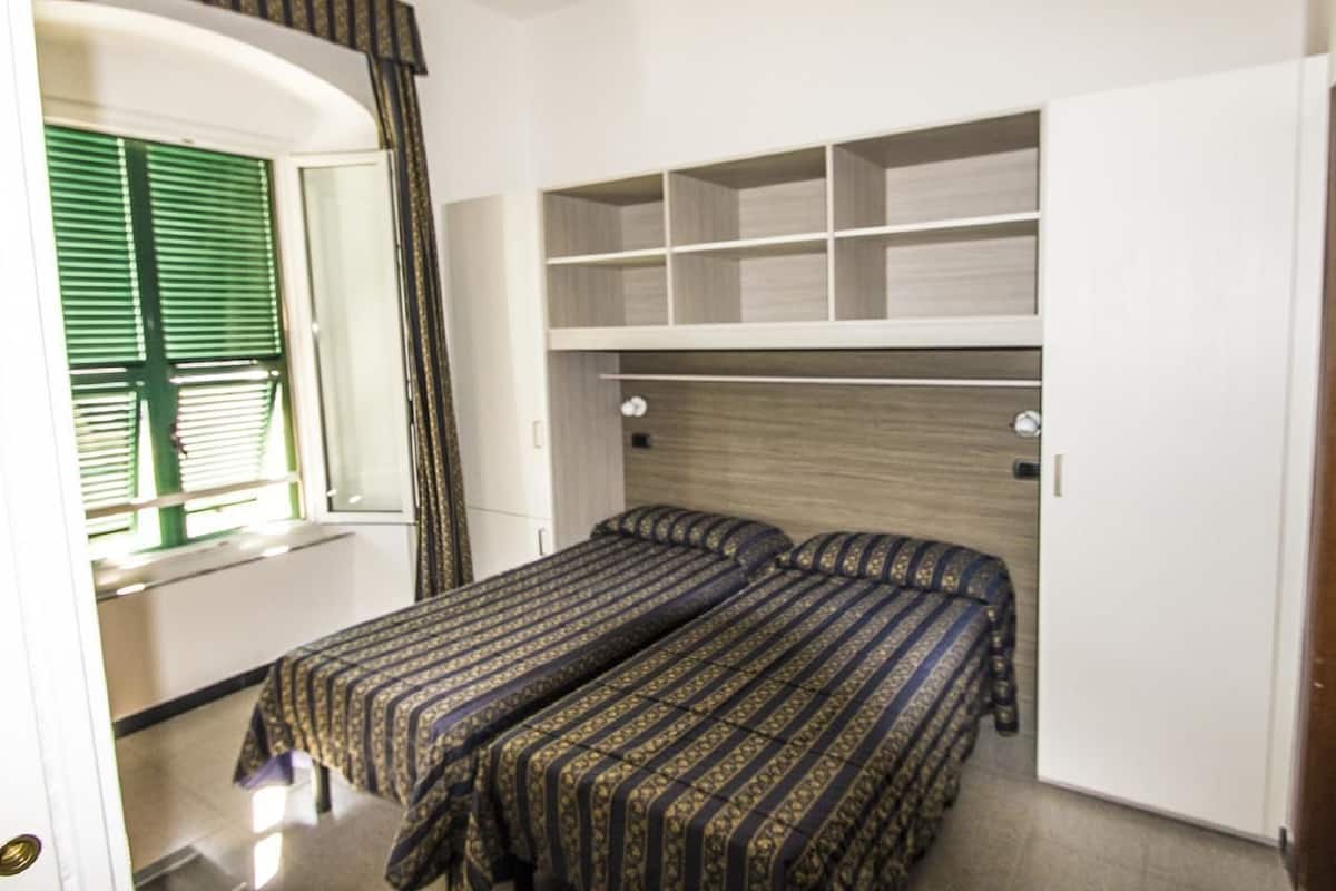 A bedroom with two beds, a built-in wardrobe, and a window with green shutters.