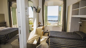 Ett hotellrum med två sängar, ett skrivbord, en stol och en TV. Det finns ett stort fönster med utsikt över havet.