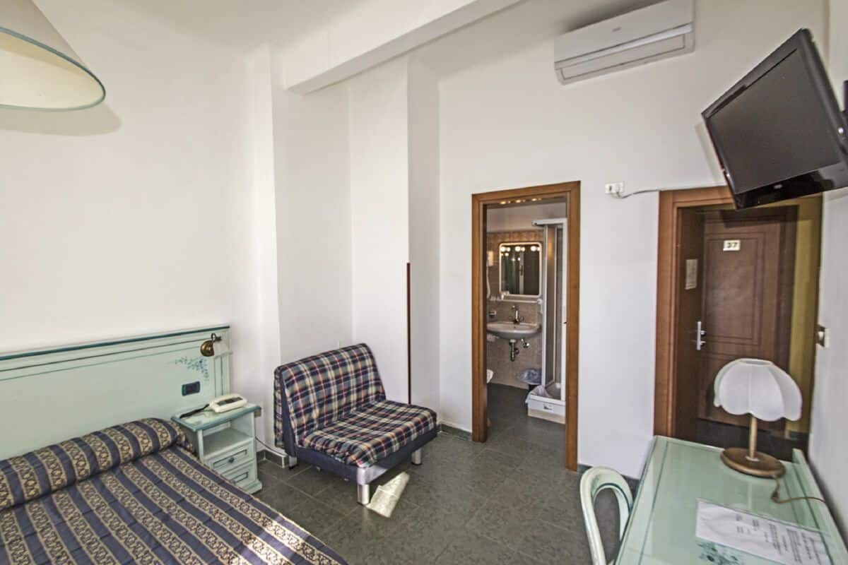 A small, compact room with a bed, a chair, a desk, and a television.