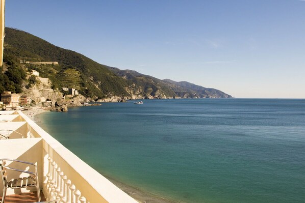 A coastal view from a balcony with a clear sea, rocky cliffs, and buildings on the hillside.