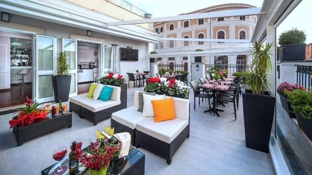 Une terrasse sur le toit avec des sièges extérieurs, un espace repas et une vue sur un bâtiment historique.