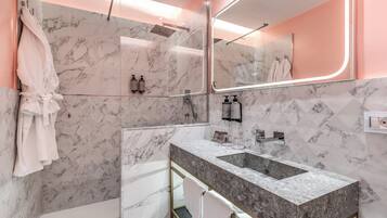 A modern bathroom with a marble wall, a large mirror, a dual sink vanity, and a glass shower enclosure.