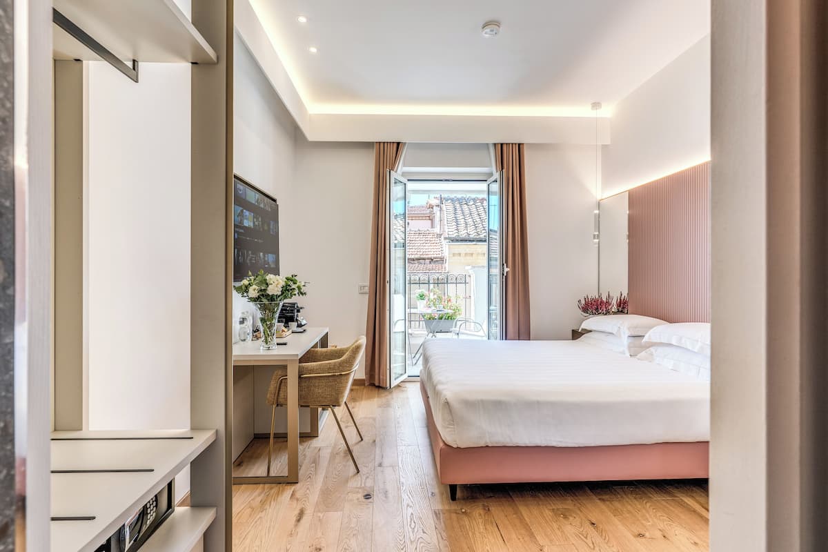 Habitación de hotel moderna con una cama grande, un escritorio con una silla y vista al exterior a través de un ventanal.