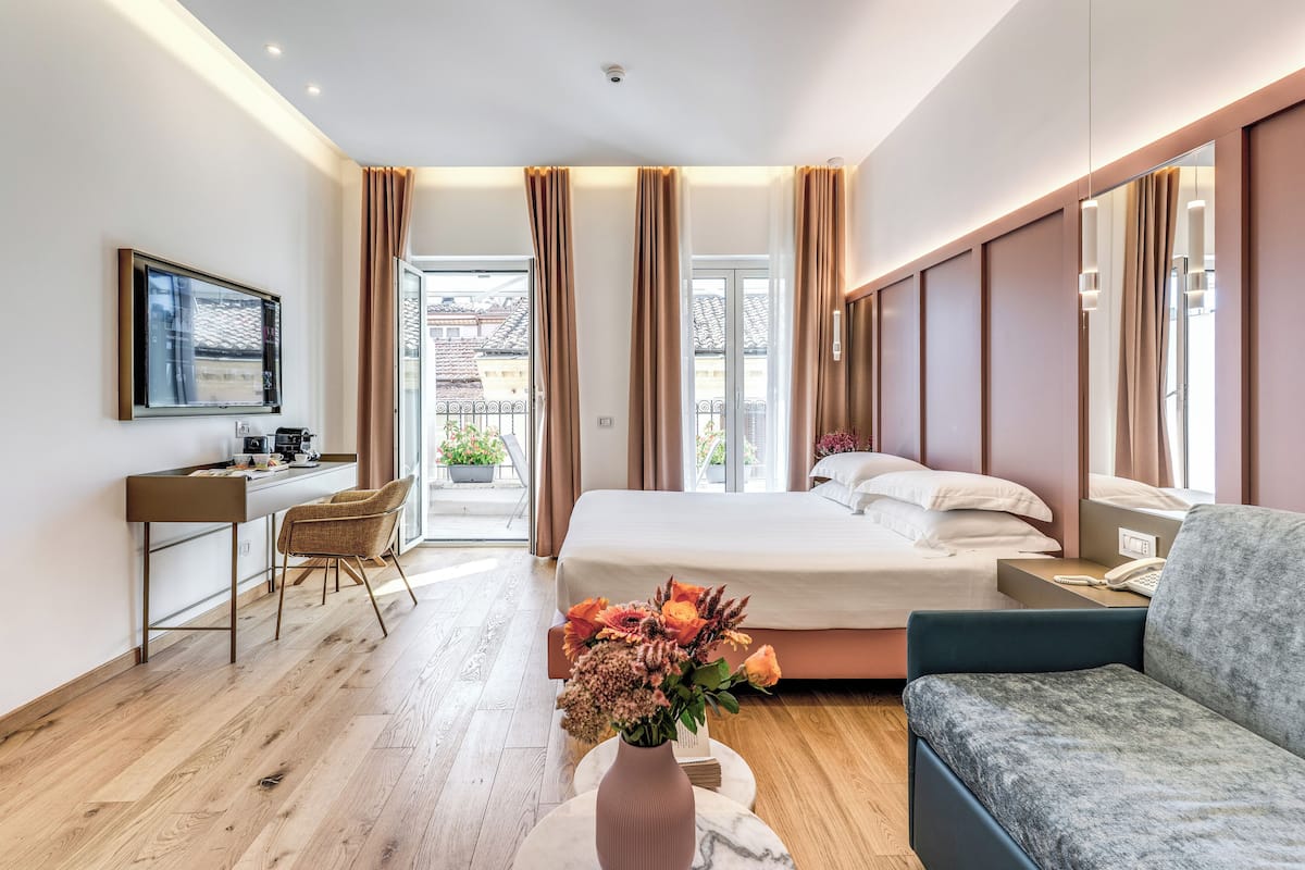 Una habitación de hotel moderna con una cama, un escritorio, una silla, un sofá y un florero con flores.