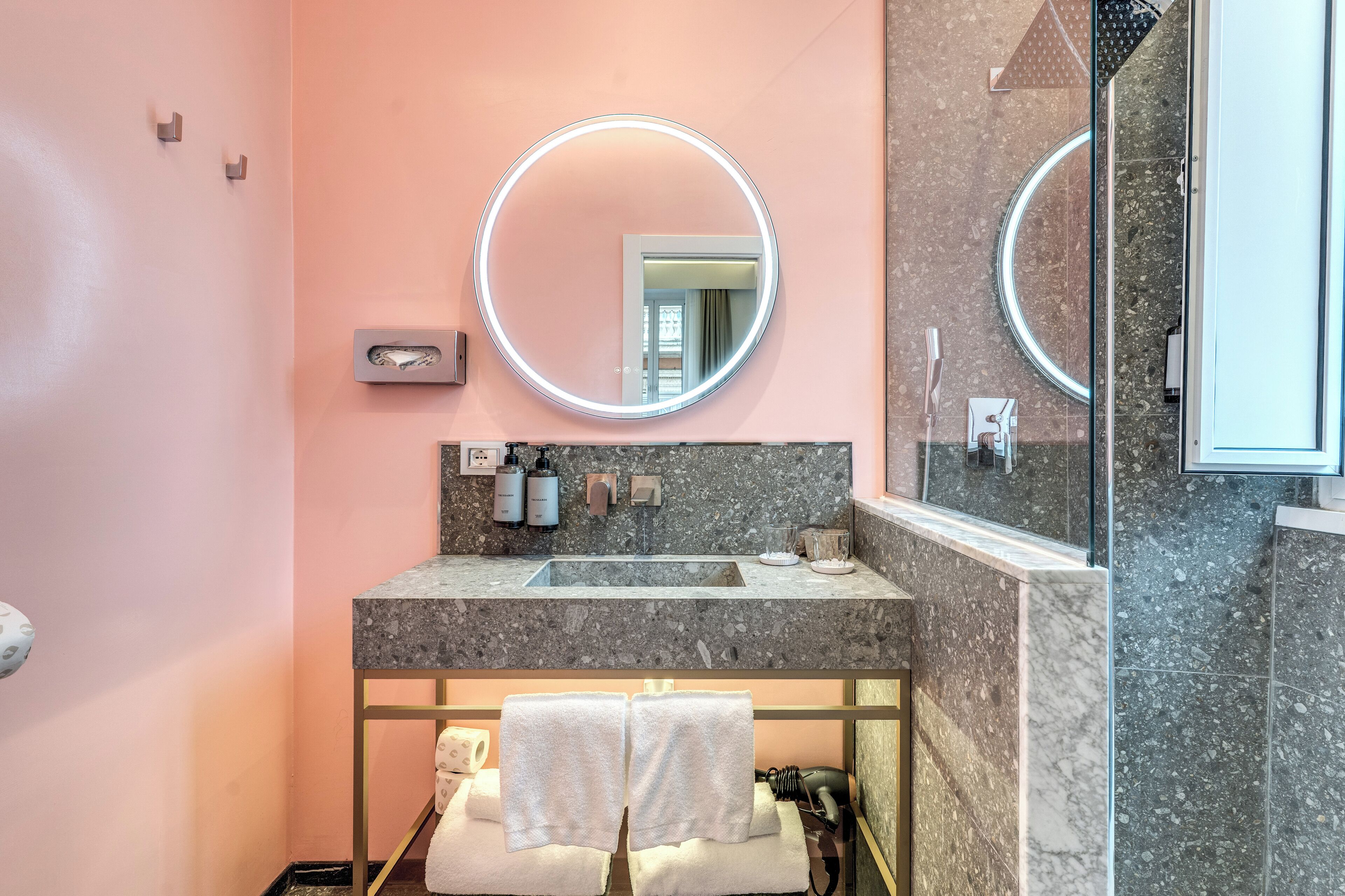A modern bathroom with a marble sink, two round mirrors, and a towel rack.
