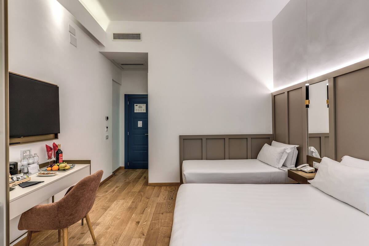 Habitación de hotel con escritorio, dos camas, una silla y televisor.