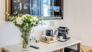 Une chambre d’hôtel équipée d’un téléviseur diffusant une chaîne de cinéma, d’un vase avec des fleurs, d’une machine à café et d’un plateau contenant des tasses à café et un menu.