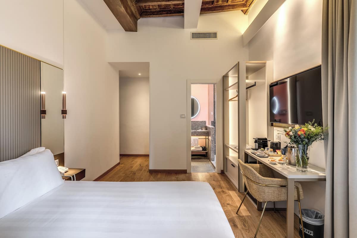 Habitación de hotel con una cama grande, un escritorio con una silla, un televisor y un baño visible a través de una puerta abierta.