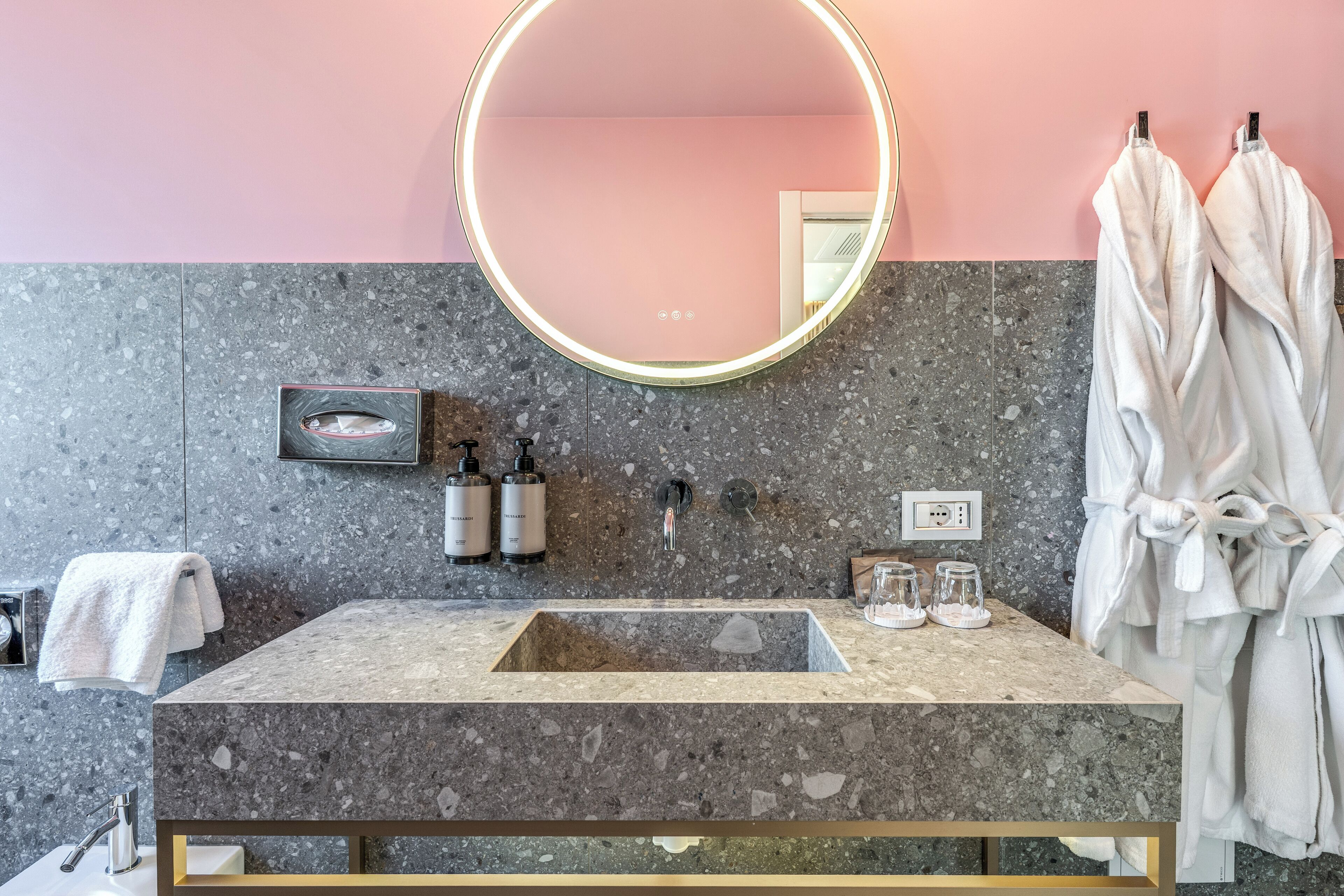 A bathroom with a marble sink, a round mirror, and two white towels.