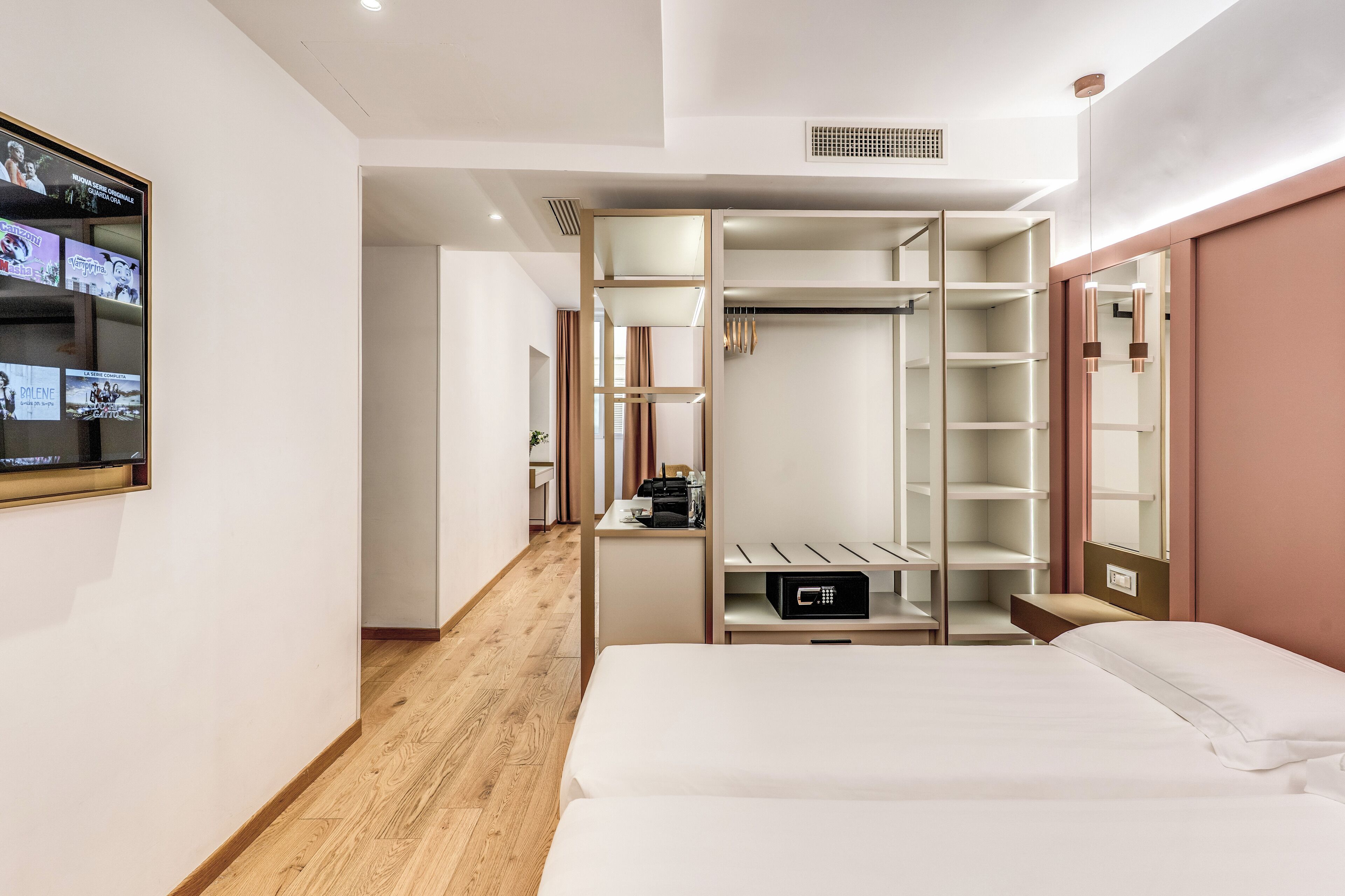 A hotel room with a bed, a desk, a wardrobe, and a TV mounted on the wall.