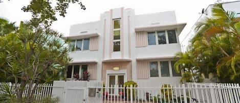 A modern two-story building with a white facade, a gated entrance, and a paved driveway.