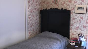 A bedroom with a single bed, a nightstand, a trash can, and a wall with floral wallpaper.