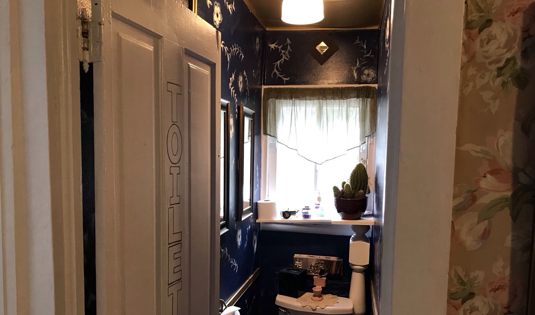 A narrow hallway with a door marked with a 'T' and a window with a curtain.
