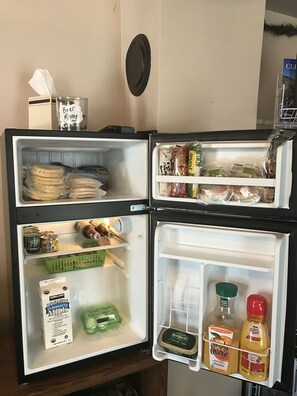A refrigerator with multiple shelves containing various food items and beverages. - Historic Windsor Hotel (Silver Plume)