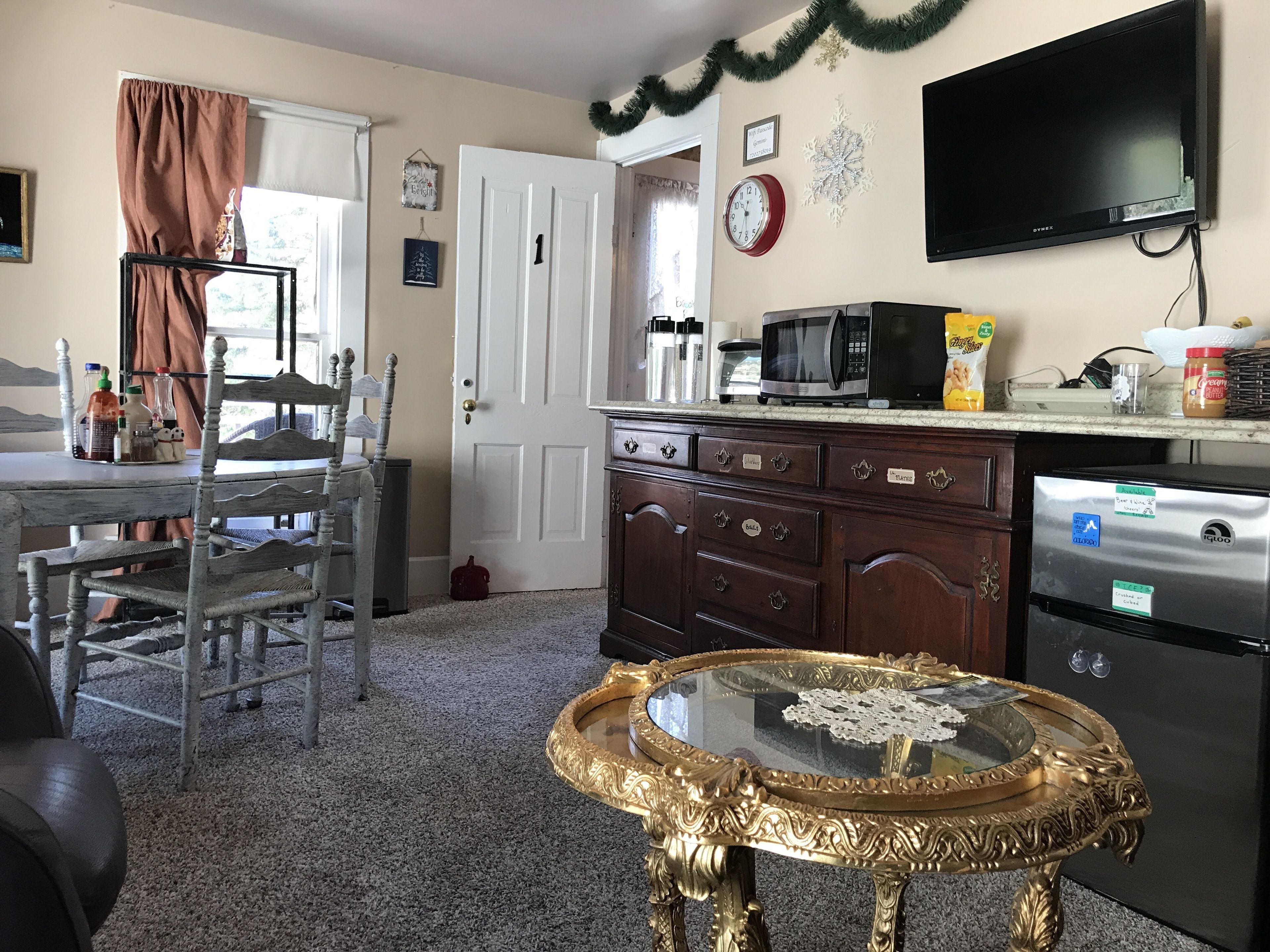 A kitchen with a dining area, a TV mounted on the wall, and a refrigerator.