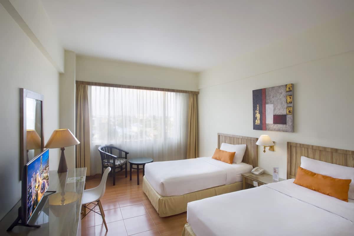 A hotel room with two beds, a desk, a chair, a TV, and a window with curtains.