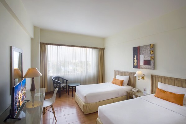 A hotel room with two beds, a desk, a chair, a TV, and a window with curtains.