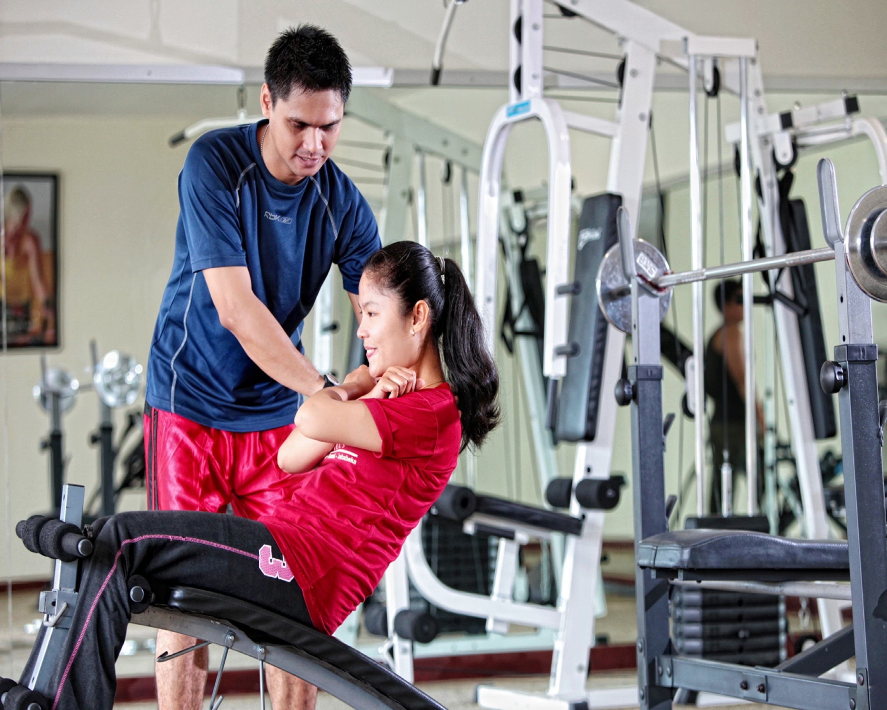 Un gimnasio con equipamiento de ejercicio y una persona ayudando a otra.