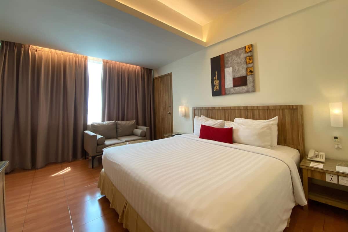 A hotel room with a large bed, a desk, a chair, and a wardrobe.