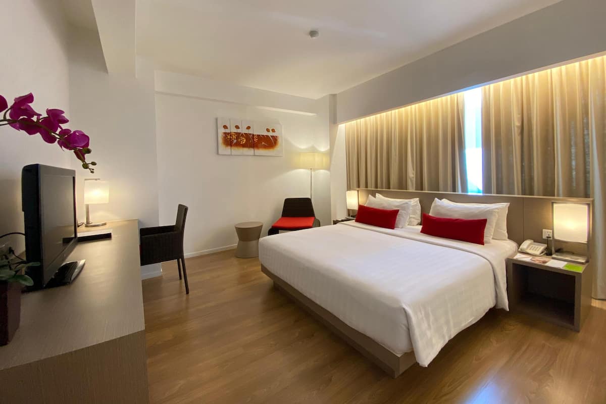 A modern hotel room with a large bed, bedside tables, a desk, a chair, and a TV.