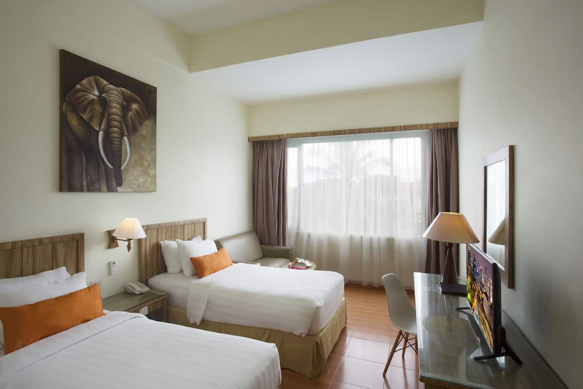 A hotel room with two beds, a desk, a TV, and a painting of an elephant.