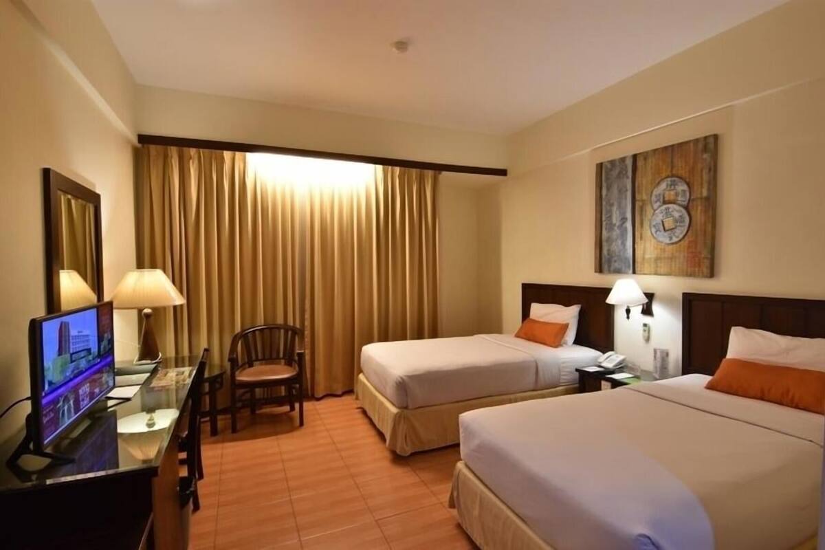 A hotel room with two beds, a desk with a TV, a chair, and a large window with curtains.
