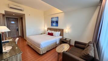 A hotel room with a bed, a desk, a chair, a sofa, and a painting on the wall.