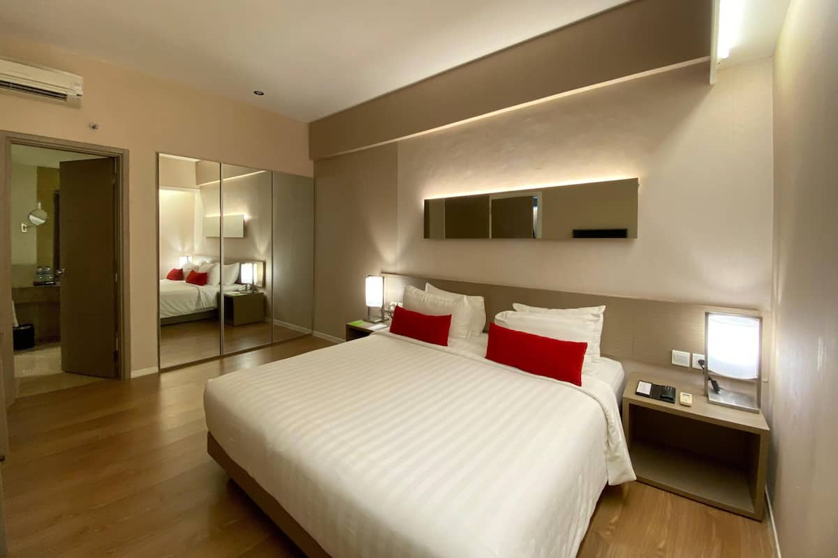 A modern hotel room with a large bed, bedside tables, a mirror, and a wall-mounted light fixture.