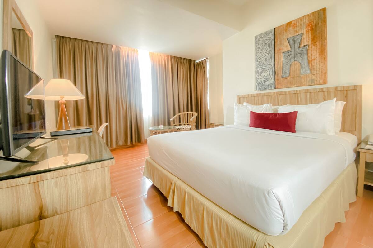 A hotel room with a large bed, a desk with a lamp, a TV, and a painting on the wall.