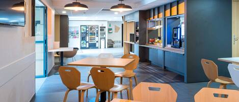 A modern dining area with wooden tables and chairs, a coffee machine, and a vending machine.