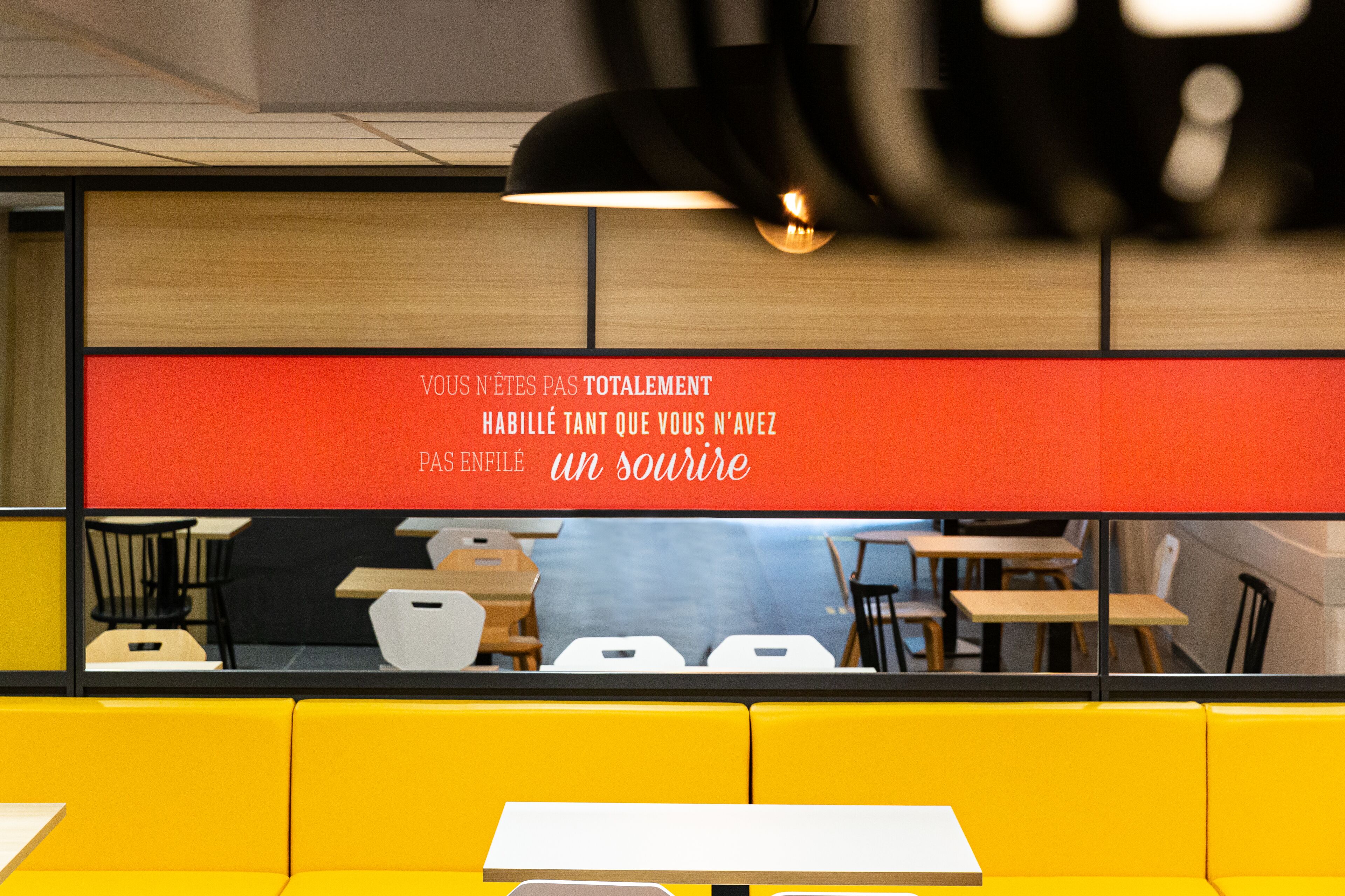 A modern restaurant interior with yellow booths, wooden tables, and a red sign with French text.