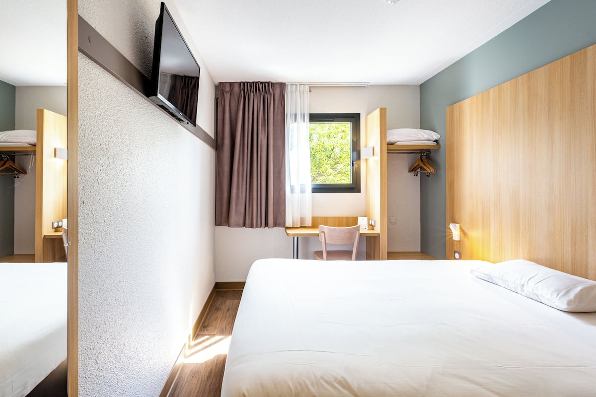 A hotel room with a bed, a desk, a chair, a TV, and a window with curtains.