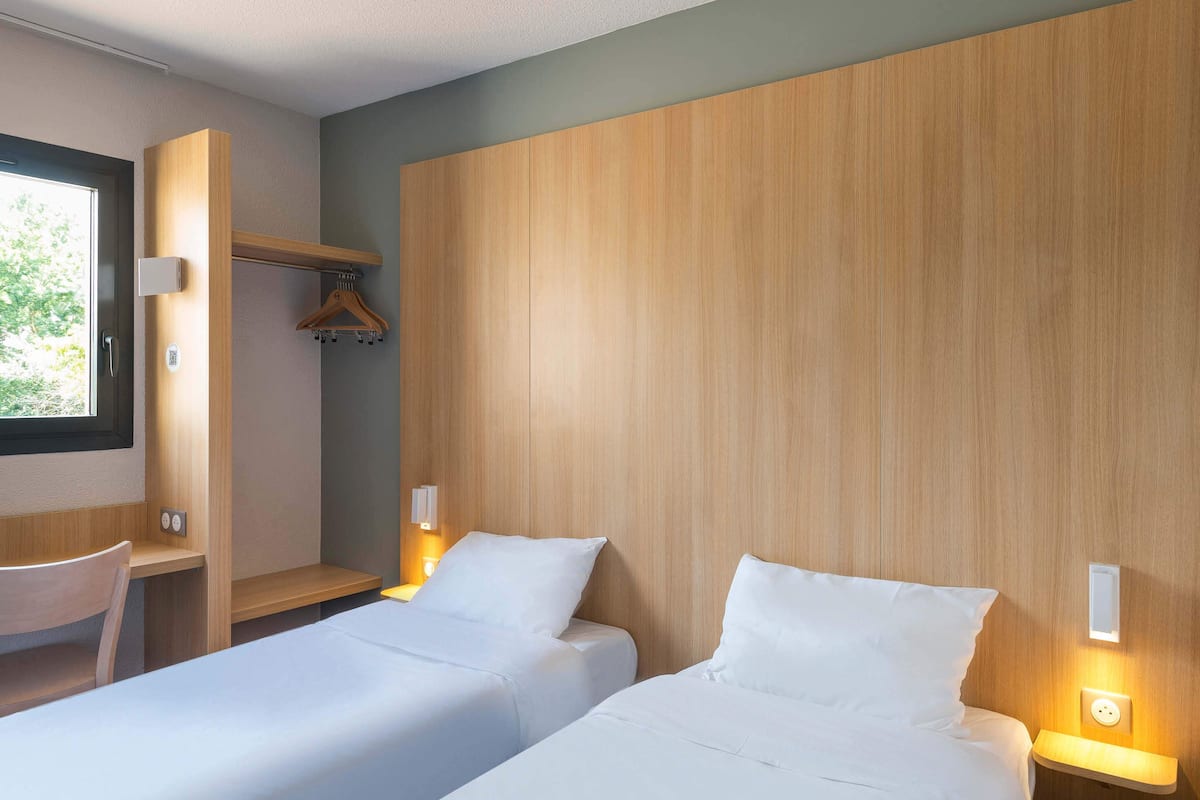 A hotel room with two beds, a desk, a chair, and a coat rack.
