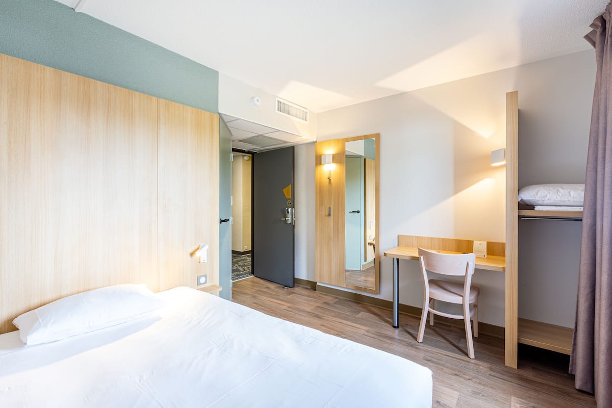 A hotel room with two beds, a desk, a chair, a mirror, and a wardrobe.