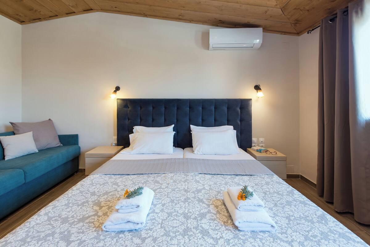 A hotel room with a large bed, two bedside tables, a blue sofa, and a wooden ceiling.