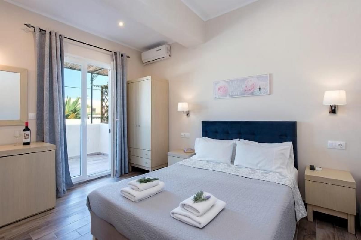 A hotel room with a bed, bedside tables, a wardrobe, and a sliding glass door to the balcony.